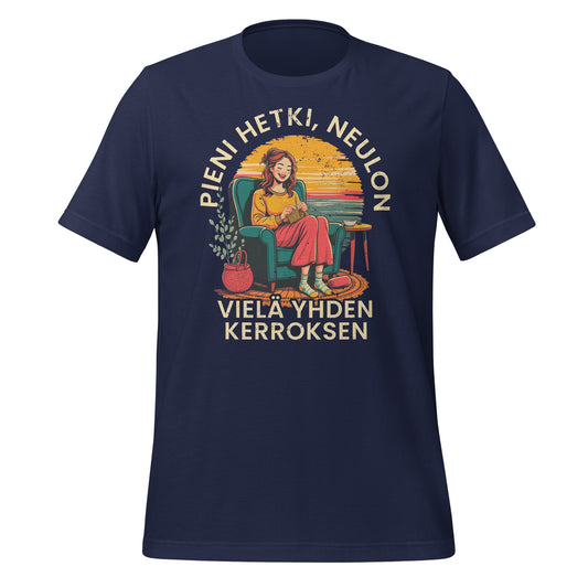 Sininen t-paita, jossa on neuloja nojatuolissa, teksti 'Pieni hetki, neulon vielä yhden kerroksen' ja kodikas design. Hyvä lahjaidea neulojille.